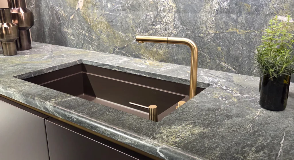 EuroCucina 2026 sink area featuring black forest green marble countertop and walls, black handleless cabinets, gold fixtures and accent strip, Salone del Mobile Milano"